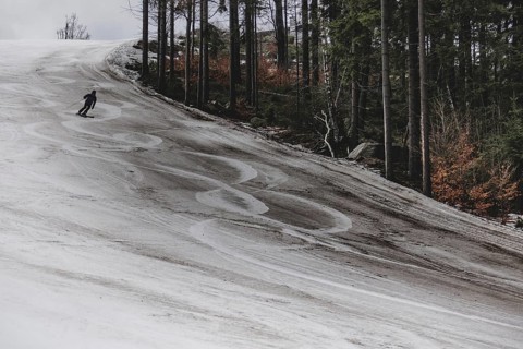A skier skis on an artificially snow-covered and dirty slope, taken on a ski slope in the Jizera