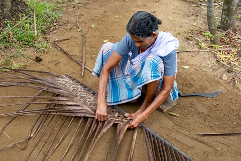 A village woman demonstrates the traditional craft of making mats from coconut leaves using her