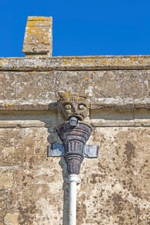 Gargoyle grotesque face drainpipe on wall medieval church of Saint John, Inglesham, Wiltshire,