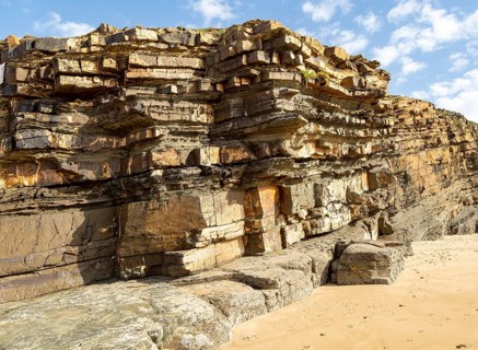 Tilted layers showing bedding planes in strata of sedimentary rock in coastal cliff at Odeceixe,