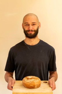 Head and shoulder portrait Caucasian white young man shaven head and beard holding fresh loaf of