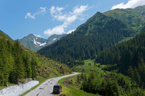 Road leading through a picturesque mountain landscape with lush greenery and clear blue skies,