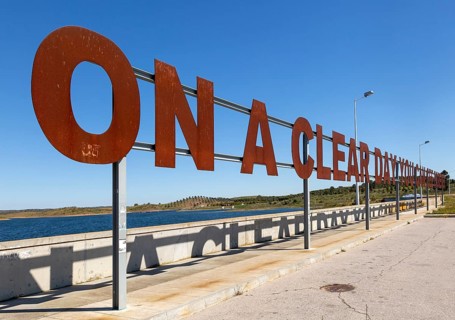 Large red rusty capital letters ON A CLEAR DAY YOU CAN SEE FOREVER blue sky background, Alqueva