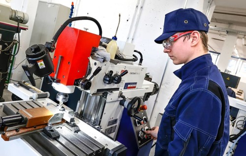 A trainee mechatronics technician works with a bench drill on a workpiece in a Deutsche Bahn