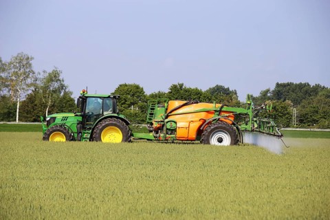 A farmer drives his tractor with a crop protection sprayer across his wheat field to combat brown