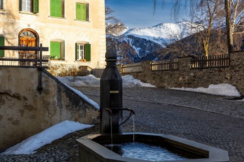Wooden fountain, house with sgraffito, facade decorations, mountain peak, snow, winter, Guarda,
