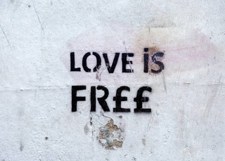 Stencilled graffito message 'Love is Free' on white wall, Newbury, Berkshire, England, UK