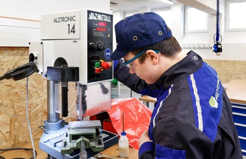 A trainee mechatronics technician works with a bench drill on a workpiece in a Deutsche Bahn