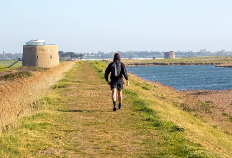 Man walking coastal path on sea wall dyke at Bawdsey, Suffolk, England, UK