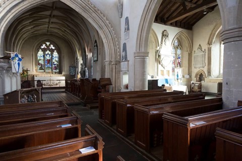 View past wooden pews through chancel arch to sanctuary and altar inside the church at Urchfont,
