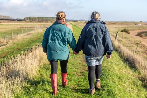 Mother and adult daughter walking together by the River Ore, Suffolk, England, UK from behind