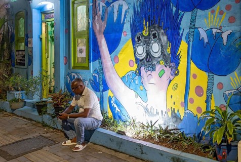 Man sits on a curb in front of illuminated street art in the streets of Fort Kochi, Cochin, Kerala,