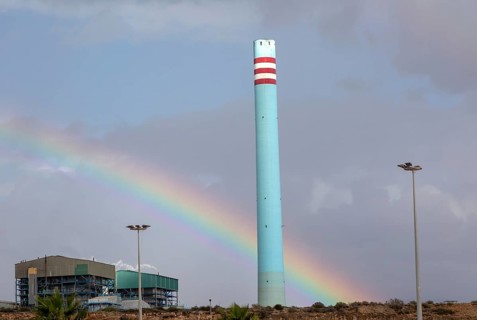 Rainbow in stormy sky behind tall blue industrial cement factory chimney, Carboneras, Almeria,