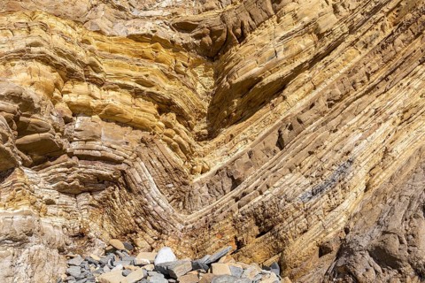 Strata of sandstone sedimentary rock in a coastal cliff with layers folded down to form a