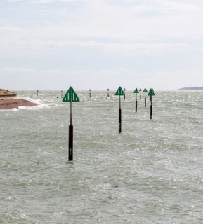 Green triangular warning markers on posts in shallow water at River Orwell river mouth, Landguard