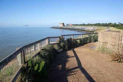 Martello tower defended by rock armour coastal defences at Bawdsey, Suffolk, England, UK calm sea