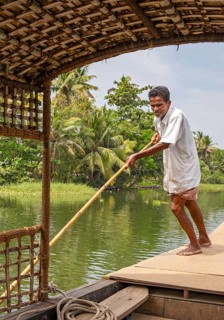 A man navigates a boat through the canals of the Kerala Backwaters using a long pole, Vembanad