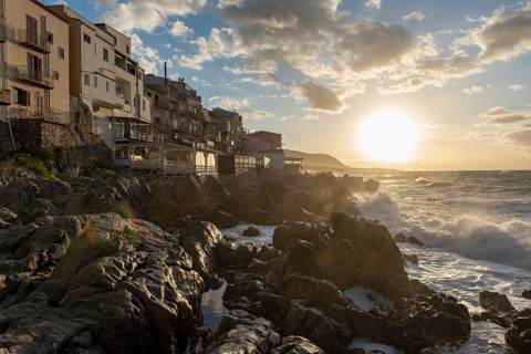 Sea water crashes against the cliffs of the rugged coastline in the town of Cefalu, Sicily, Italy,