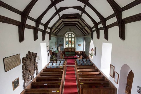 Raised angle view looking east down the nave towards the altar and east window with wooden pews,