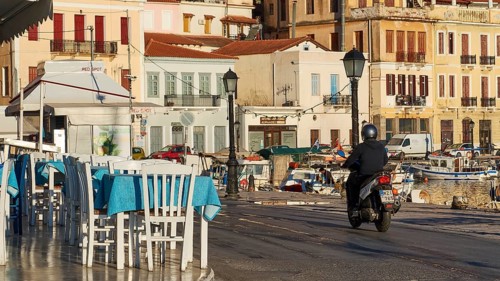 A scooter rides early in the morning at a cafe along the coastal road overlooking the sea, Gythio,