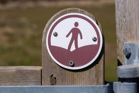 Macro close up of figure walking footpath sign on fencepost, Sutton, Suffolk, England, UK