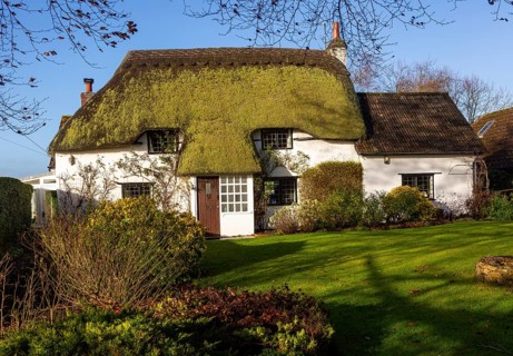 Pretty thatched country cottage home with green moss growing on thatch, Cherhill, Wiltshire,