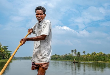 A man navigates a boat through the canals of the Kerala Backwaters using a long pole, Vembanad