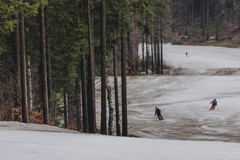 Skiers skiing on an artificially snow-covered and dirty slope, taken on a ski slope in the Jizera