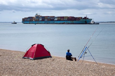 Fisherman watches arrival of Maersk Utah container ship at Port of Felixstowe, Suffolk, England, UK