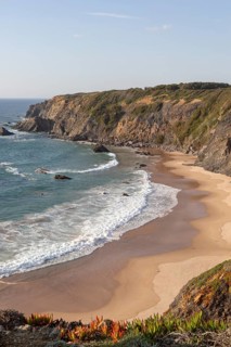 Secluded sandy beach in bay between rocky headlands at Parque Natural do Sudoeste Alentejano e