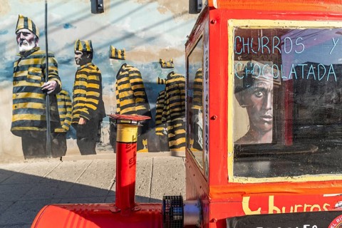 Red trolley for selling churros, behind a graffito with men in convict clothing, Ushuaia, Tierra