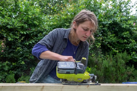 Young woman using electric power sawing tool without safety googles or protective clothing, model