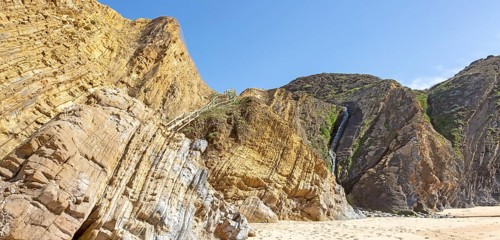 Folded sedimentary rock strata dipping downwards in cliff at Praia dos Alteirinhos, Zambujeira do