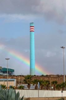 Rainbow in stormy sky behind tall blue industrial cement factory chimney, Carboneras, Almeria,