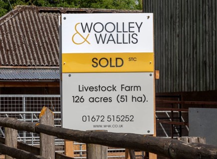 Estate agent Woolley and Wallis property sold sign at livestock farm near Potterne, Wiltshire,