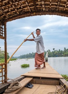 A man navigates a boat through the canals of the Kerala Backwaters using a long pole, Vembanad