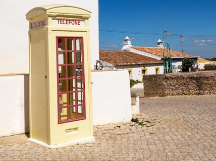 Old fashioned Telephone Telefone box kiosk in street of traditional Portuguese village, Cacela