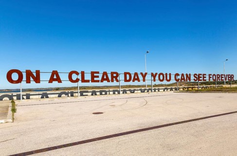 Large red rusty capital letters ON A CLEAR DAY YOU CAN SEE FOREVER blue sky background, Alqueva
