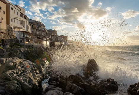 Sea water crashes against the cliffs of the rugged coastline in the town of Cefalu, Sicily, Italy,