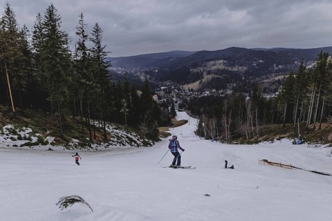 Skiers skiing on an artificially snow-covered and dirty slope, taken on a ski slope in the Jizera