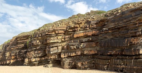 Tilted layers showing bedding planes in strata of sedimentary rock in coastal cliff at Odeceixe,