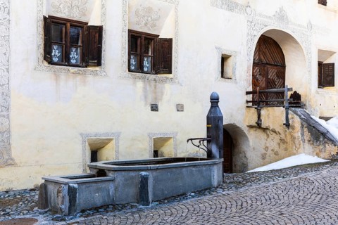 Wooden fountain in front of a historic house, sgraffito, facade decorations, Guarda, Engadin,