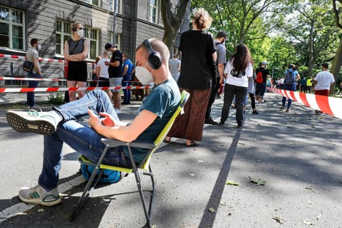 A vaccinated person sits on his folding chair in a long queue. Neighbourhood residents in the