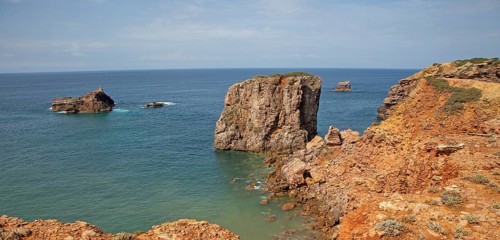 Coastal stacks and stumps orange coloured crumbling cliffs rise from Atlantic Ocean at Cabo de Sao