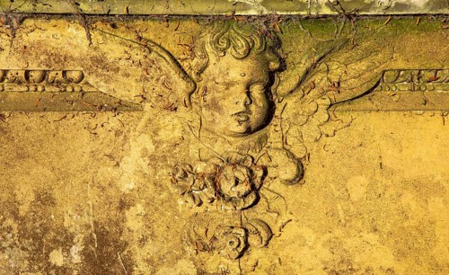 Close up of stonework carving of cherub angel face and wings on gravestone, UK