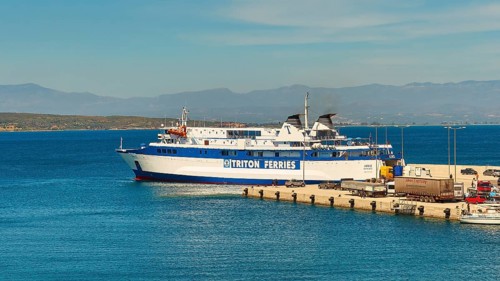 Ferry in the harbour loaded with trucks, surrounded by sea and mountains under a blue sky, Gythio,