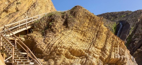 Folded sedimentary rock strata dipping downwards in cliff at Praia dos Alteirinhos, Zambujeira do