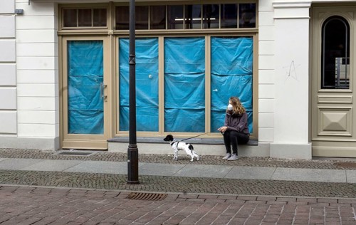 A woman sits with her dog in front of a closed shop. Customers who want to buy in retail stores in