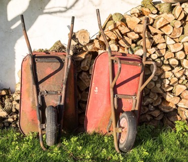 Two old red metal wheelbarrows leaning against pile wood logs in garden, Cherhill, Wiltshire,