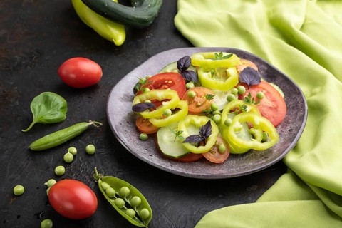 Vegetarian salad from green pea, tomatoes, pepper and basil on a black concrete background and